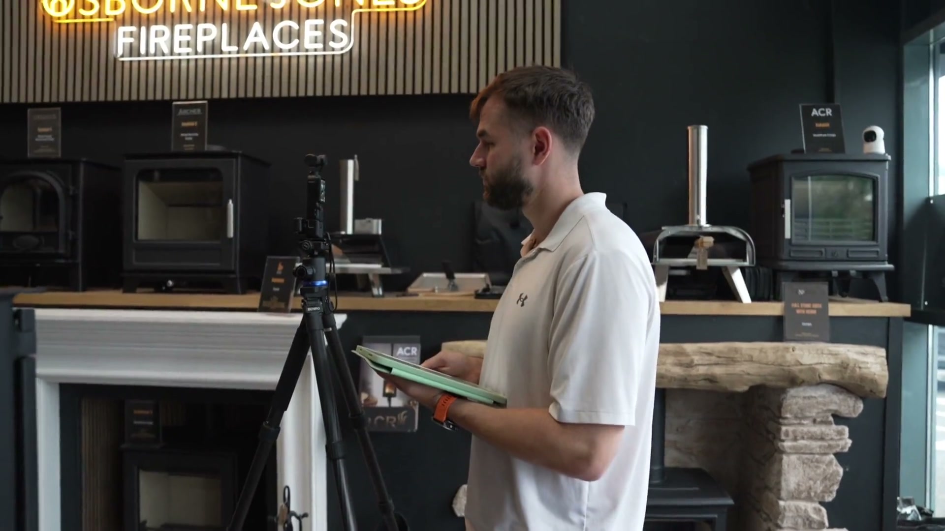 Luke Watkins filming in the Osborne Jones Fireplaces showroom, a camera on a tripod beside him