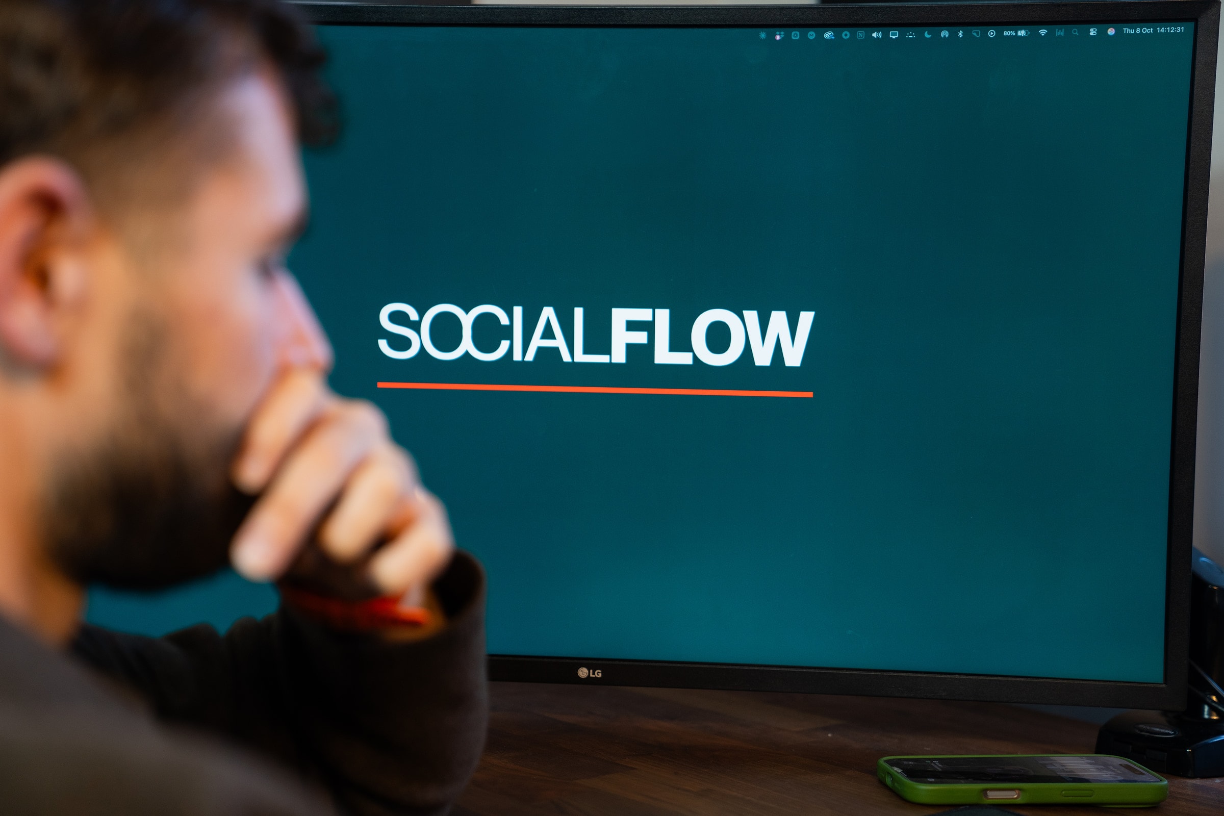Luke Watkins at his desk, the Social Flow logo on the screen in front of him